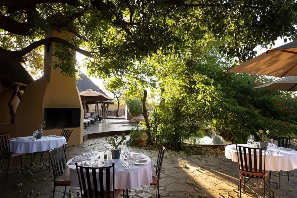Shaded outdoor table setting for dinner ,with fireplace and pool in the background.