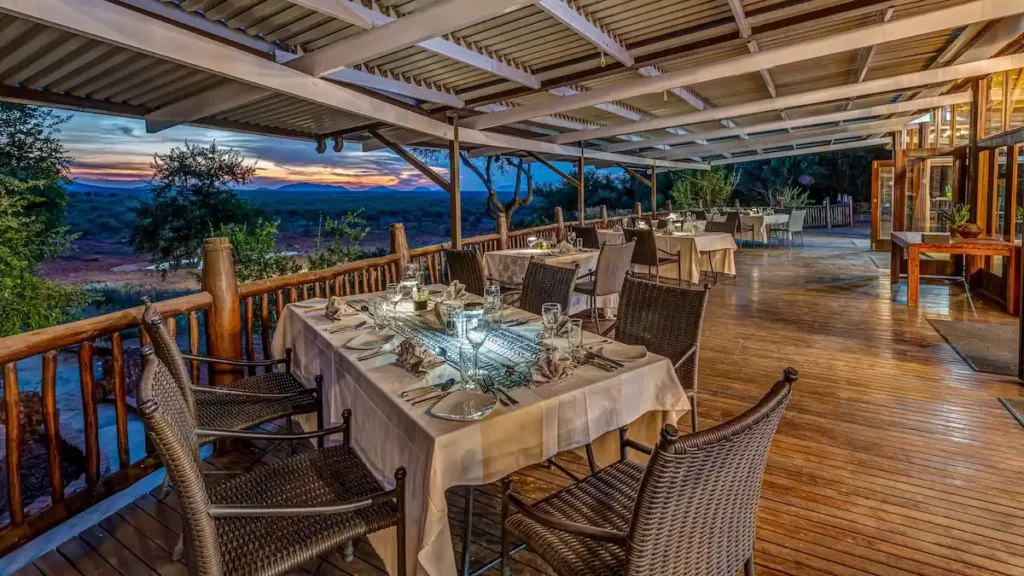 Elegant evening dining setting on a covered deck overlooking a waterhole with a sunset view.