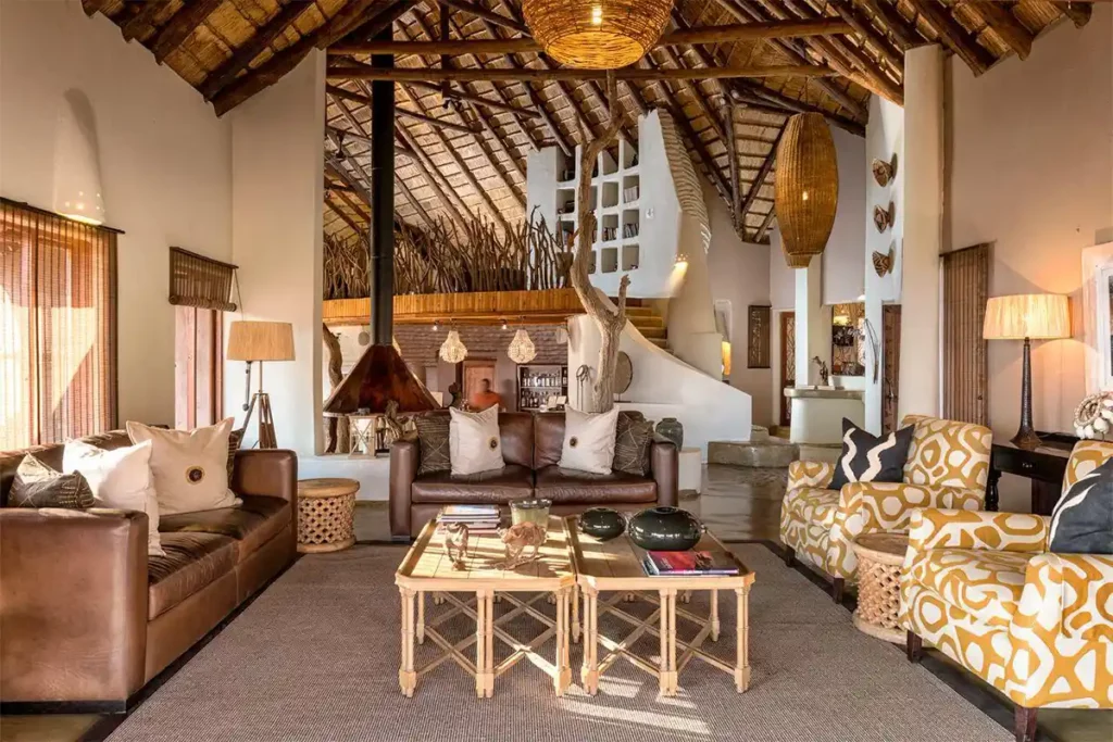 Thatched guest lounge area with sofas, rustic furnishings, fireplace and African inspired decor.