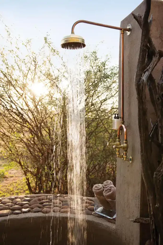 Rustic outdoor shower with bathroom amenities and bushveld views.
