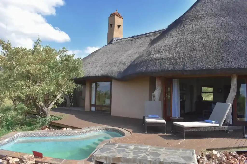 Exterior view of thatched suite with deck, plunge pool, loungers, and bush views.